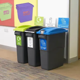 Three dark grey recycling bins with different colored lids (light green for mixed recycling, black for general waste, and blue for confidential paper) stand in a row with corresponding labelled signs above them.