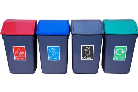 A line of four dark grey bins with angled lids – red for plastics, blue for paper, dark grey for general waste, and green for mixed recycling – each labelled with an icon and text.