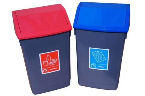 Two dark grey bins with angled lids are shown side-by-side: one with a red lid and a "plastics" label, the other with a blue lid and a "paper" label, both featuring recycling icons.